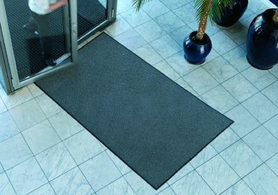Worker cleaning rubber matting in a busy industrial workplace with safety equipment