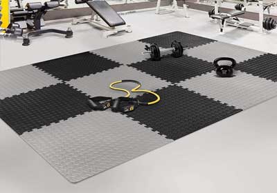 Rubber gym mats and interlocking tiles neatly installed in a UK home gym setup with weights and equipment