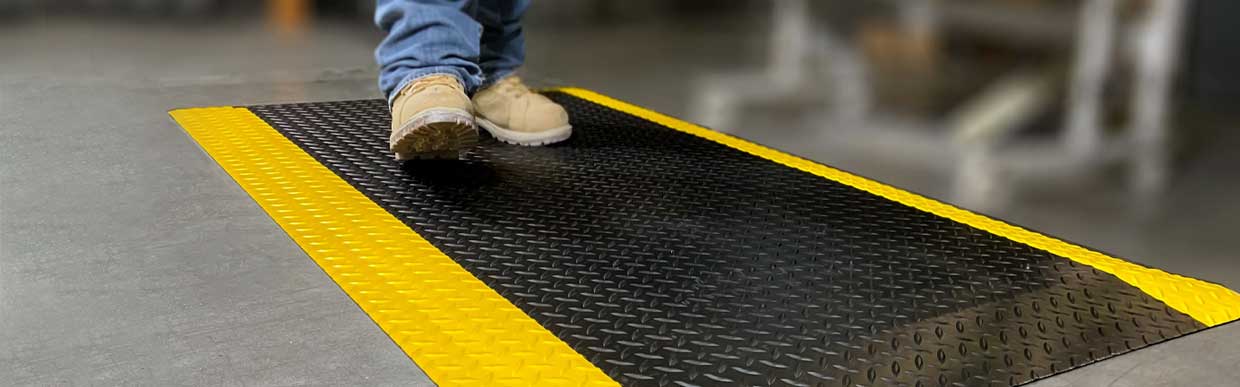 Worker standing on anti-fatigue rubber matting in a factory to reduce workplace fatigue and joint stress
